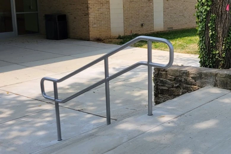 Photo of silver metal pipe railing on an outdoor concrete staircase